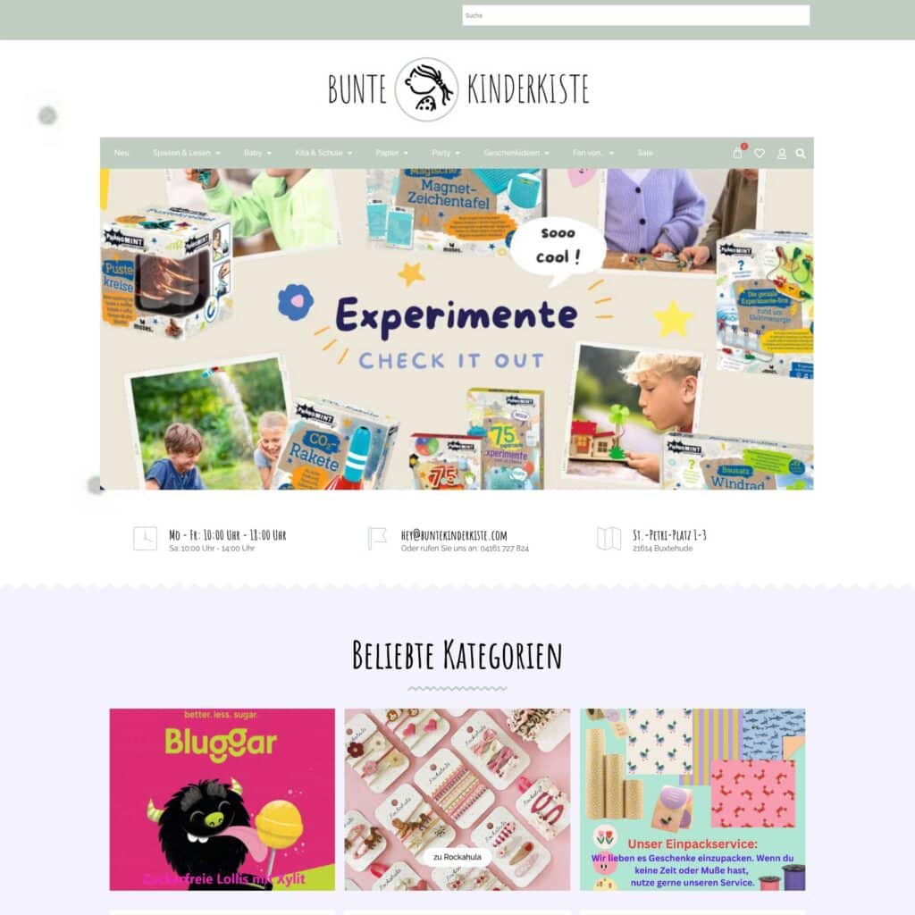 Screenshot der Homepage der Bunten Kinderkiste mit lehrreichen Experimentierkästen, verspielten Grafiken, Navigationsmenü, Kontaktinformationen, Öffnungszeiten und Rubriken für beliebte Kategorien wie Bluggar, Spiele und Kreativsets.